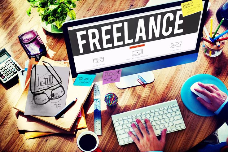 Freelance digital marketer workspace with computer displaying freelance work, keyboard, notes, and marketing tools